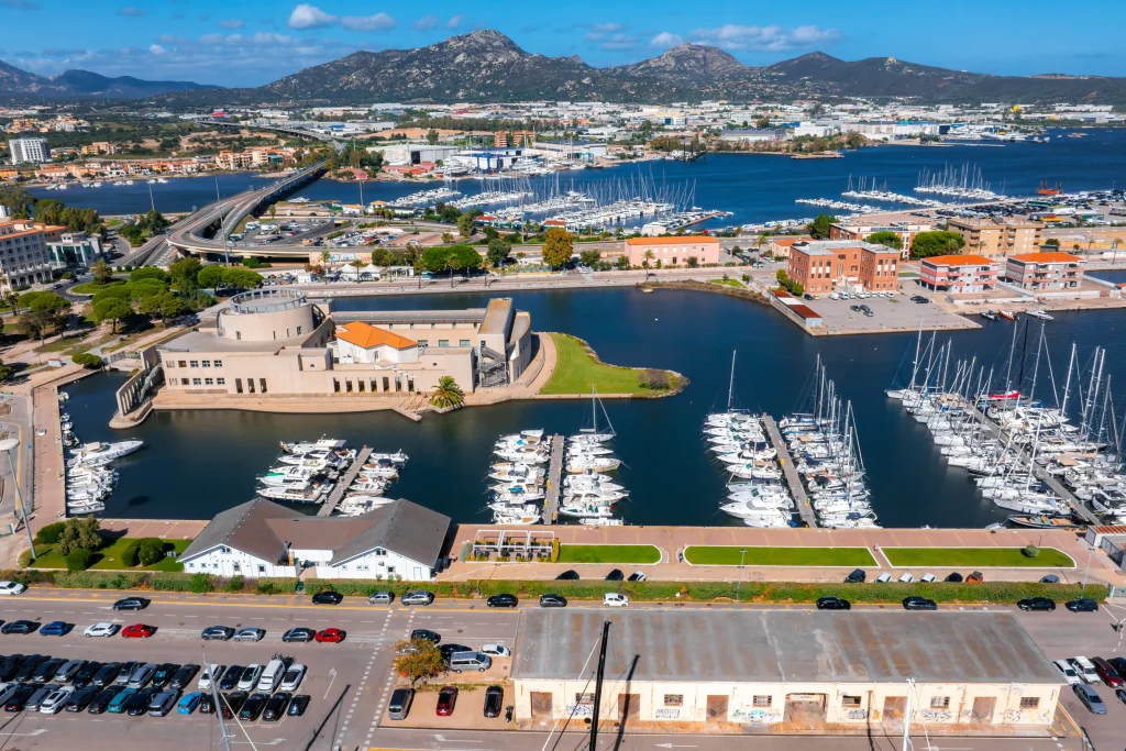 Aerial of Olbia waterfront museum, marina pontoons, city and mountains behind
