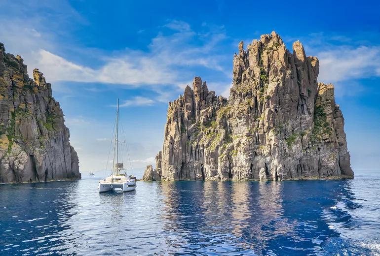 A catamaran anchored beside towering volcanic sea stacks in the Aeolian Islands