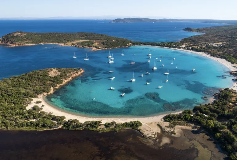 Aerial of a horseshoe-shaped bay with anchored yachts and a white sand beach