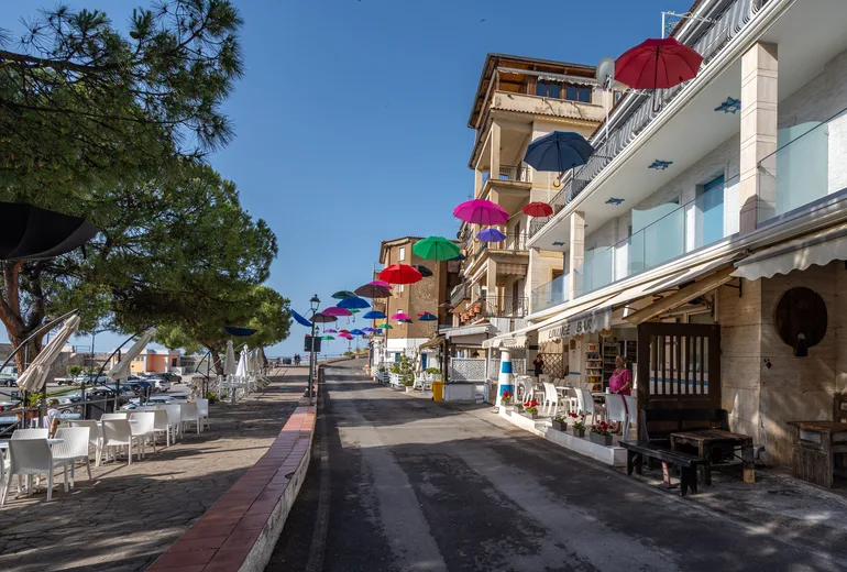 Cafe-lined seafront street with colorful umbrellas strung overhead