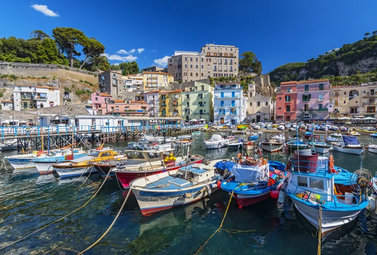 Colorful fishing boats moored at Marina Grande harbor below pastel houses in Sorrento