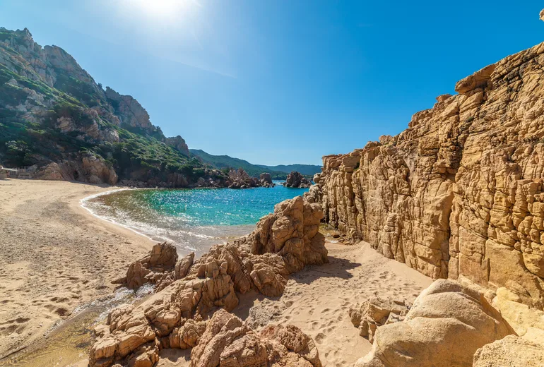 Golden rock formations framing a small sandy cove with clear water