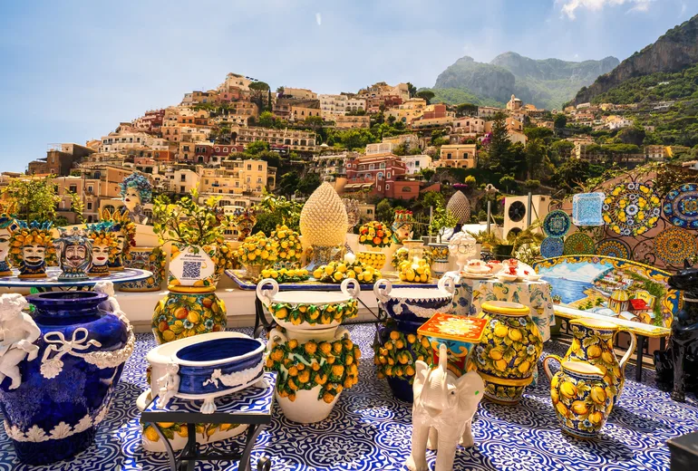 Hand-painted ceramic pottery displayed on a terrace overlooking Positano hillside houses