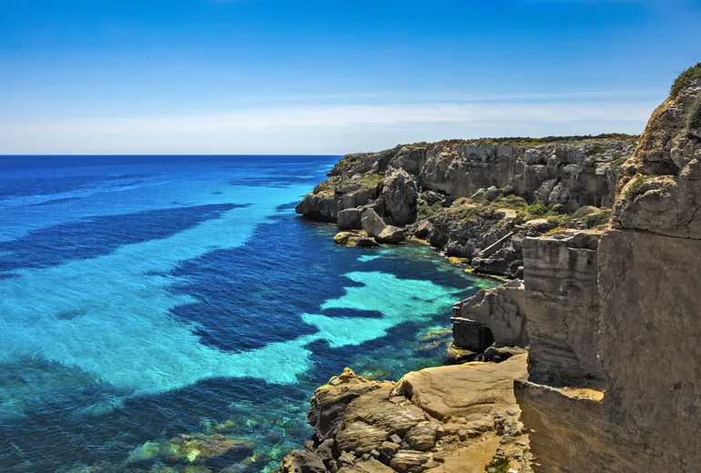 Limestone sea cliffs and vivid turquoise shallows under a clear sky