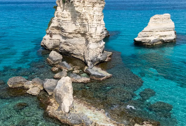 Limestone sea stacks rising from clear turquoise water off a rocky shoreline