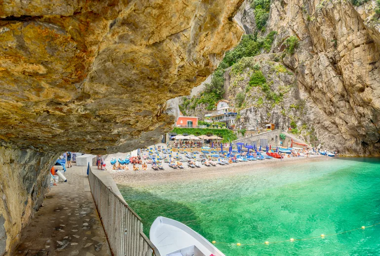 Pebble beach cove crowded with umbrellas beneath cliffs at Marina di Praia, Praiano