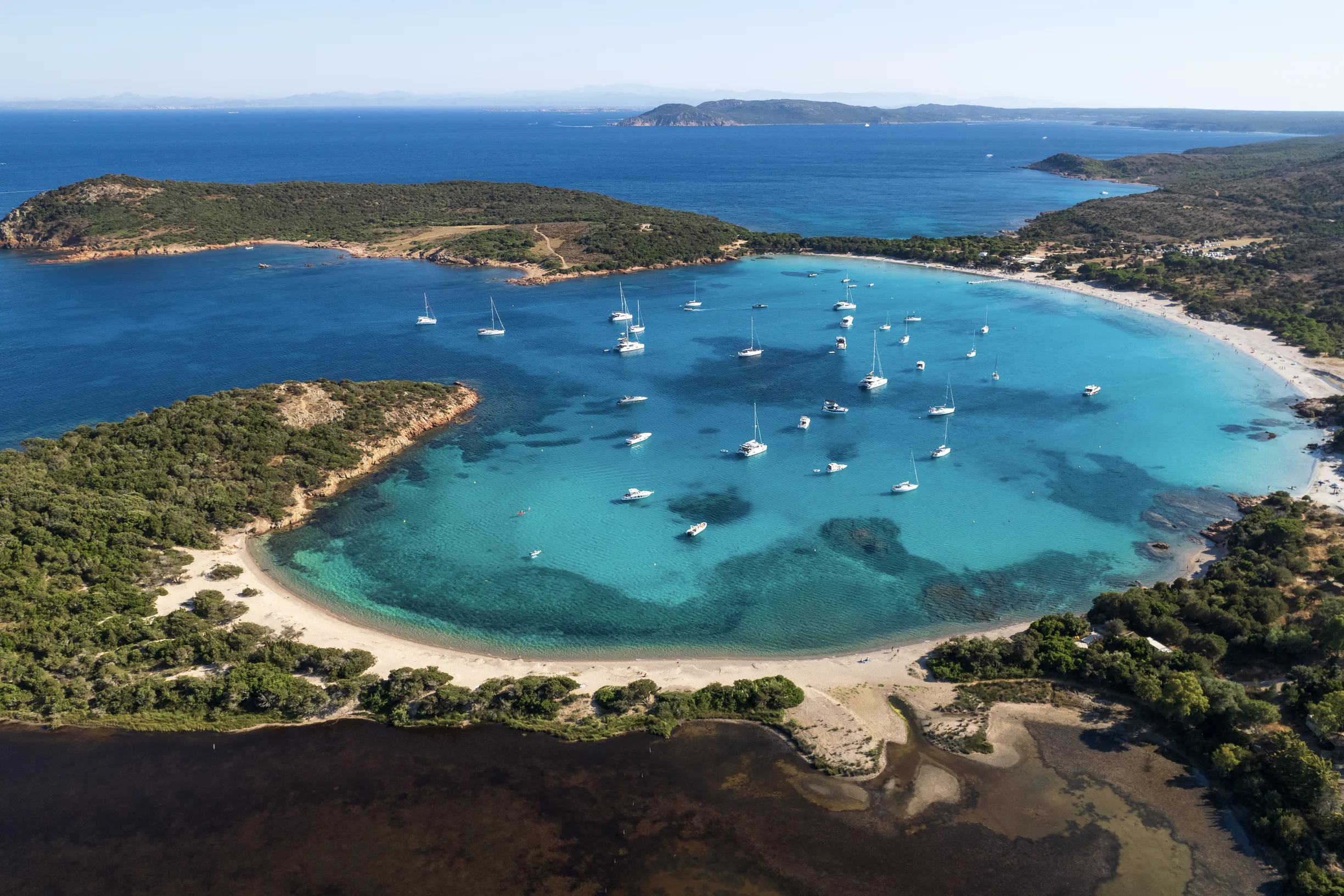 Aerial of horseshoe-shaped bay with anchored yachts and white sand beach