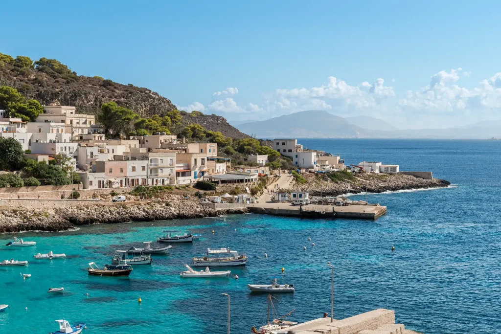 Whitewashed Levanzo village above clear cove with small boats, Egadi Islands
