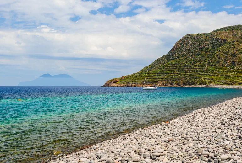Sailboat off a pebble beach with an Aeolian island on the horizon