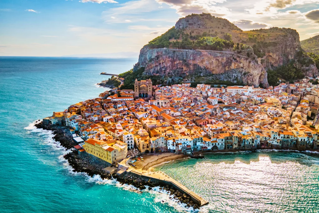 Aerial view of Cefalu old town rooftops beneath La Rocca crag, Sicily