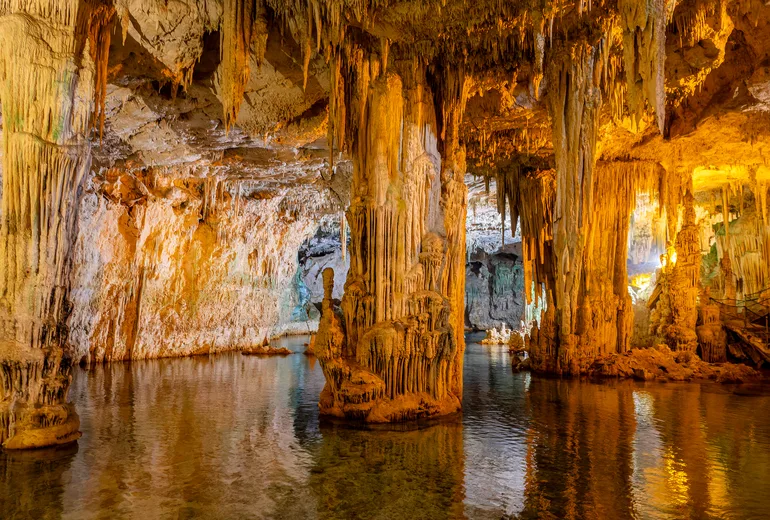 Stalactite columns reflected in still water inside a coastal sea cave