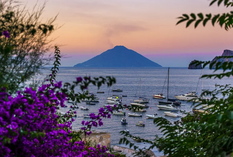 Stromboli volcano at dusk framed by bougainvillea with anchored boats