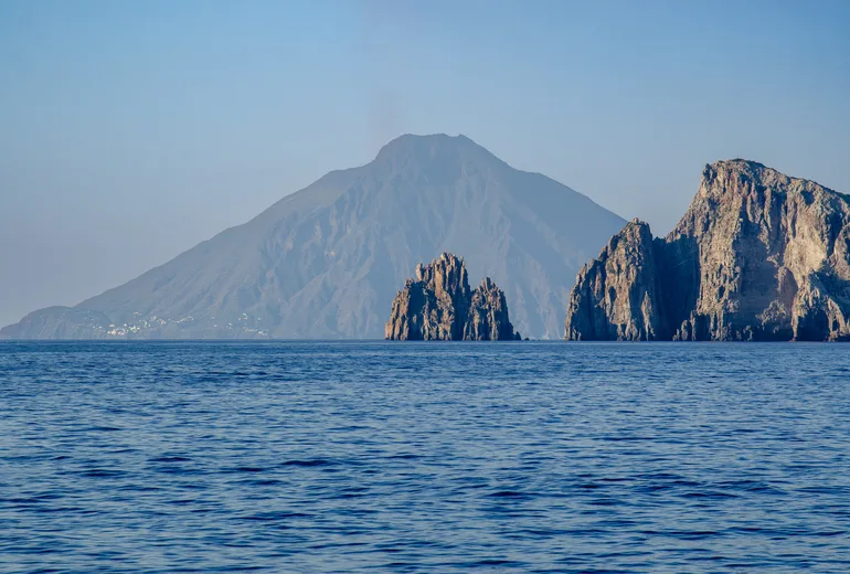 Volcanic island cone rising over a calm sea beyond rugged coastal cliffs